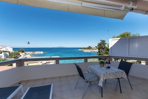 Een balkon met een tafel en stoelen, met uitzicht op de kust onder een heldere lucht.