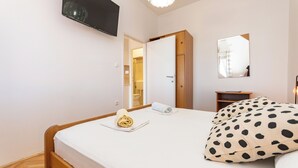 Habitación de hotel con cama, televisión montada en la pared, armario de madera, espejo y mesita de noche pequeña.