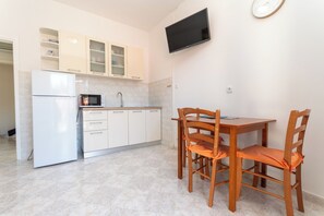 Eine Küche mit Kühlschrank, Mikrowelle und Schränken, ein Esstisch mit Stühlen sowie ein an der Wand montierter Fernseher.