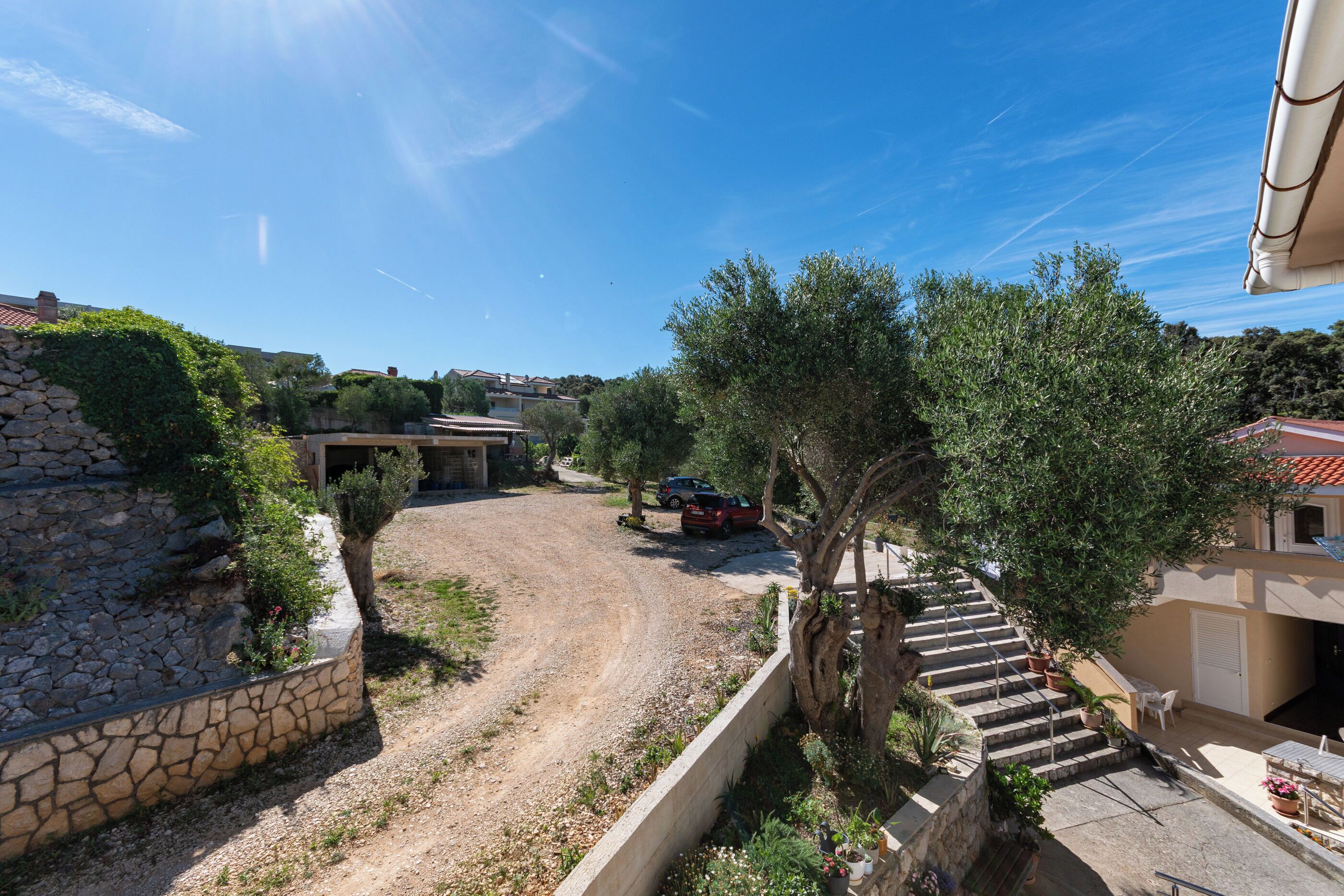 Ein Wohngebiet mit einem Feldweg, Steinmauern und einer Treppe, die zu einem Gebäude mit einem Balkon führt.