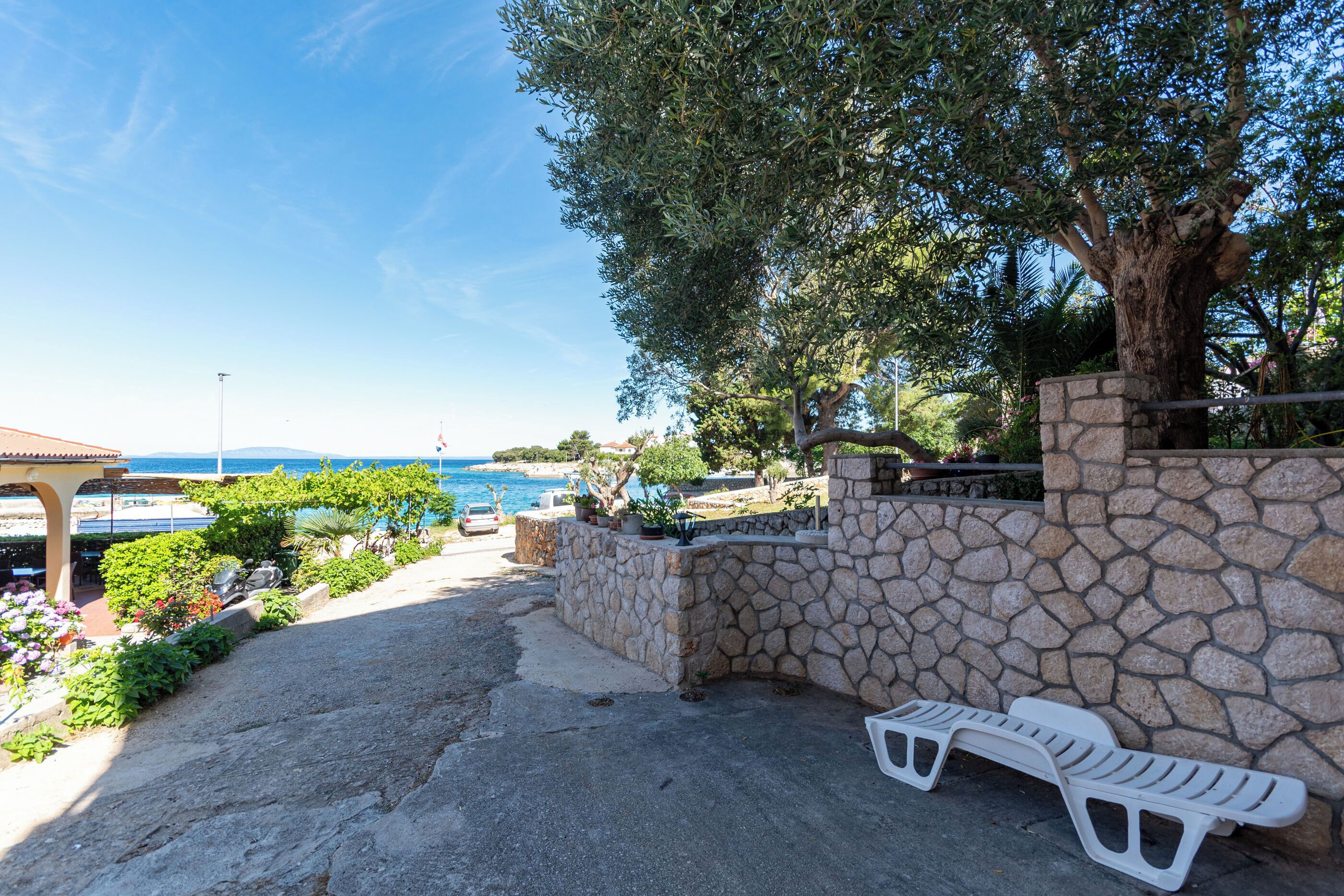 A stone wall, a white lounge chair, and a view of the sea.