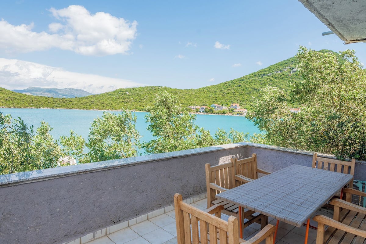 A terrace with a table and chairs overlooking a body of water and greenery.