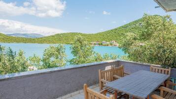 Terraza con mesa y sillas con vistas a un cuerpo de agua y follaje.