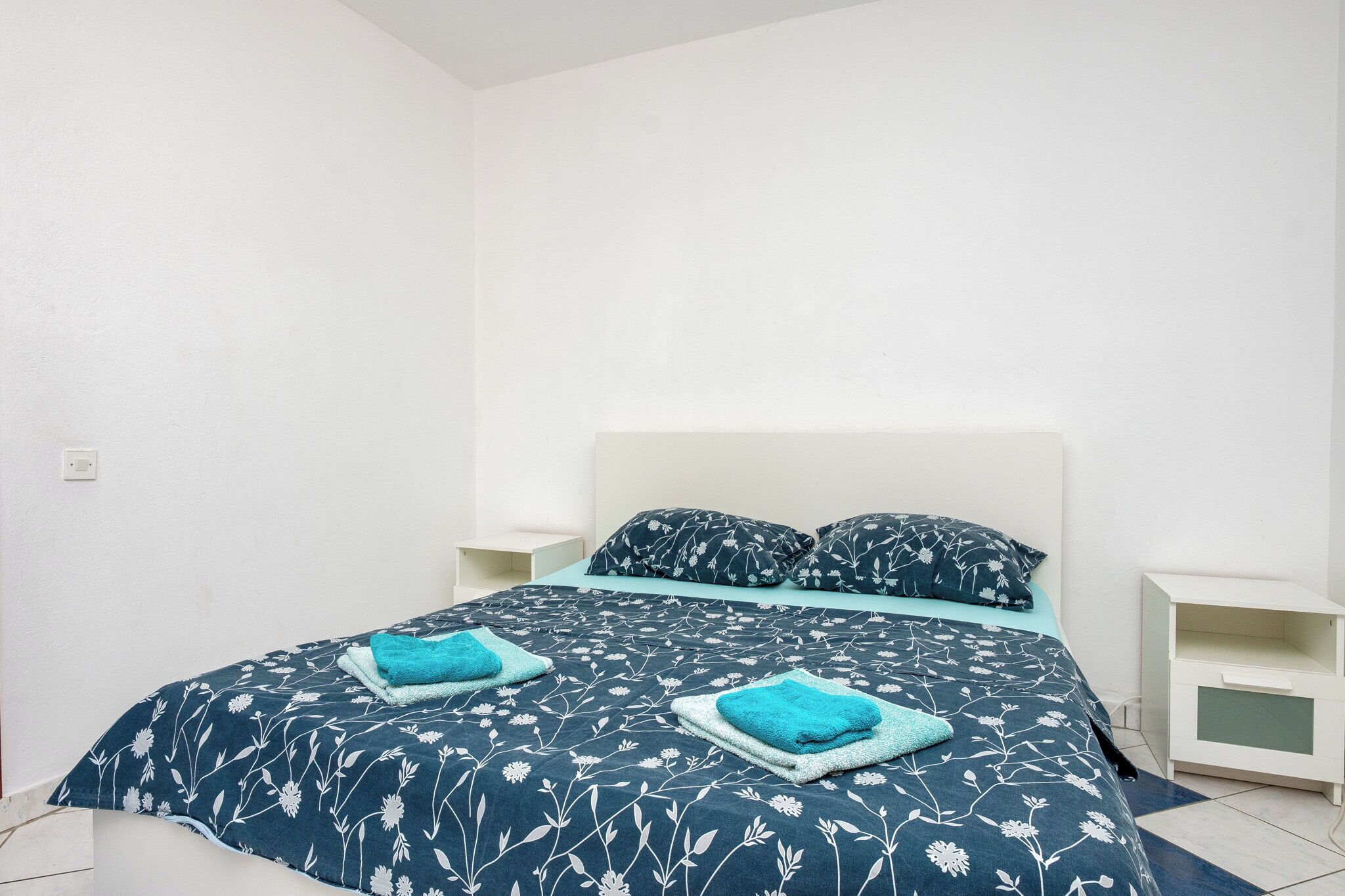 Una cama con una colcha estampada con motivos florales, dos almohadas y dos toallas a juego.