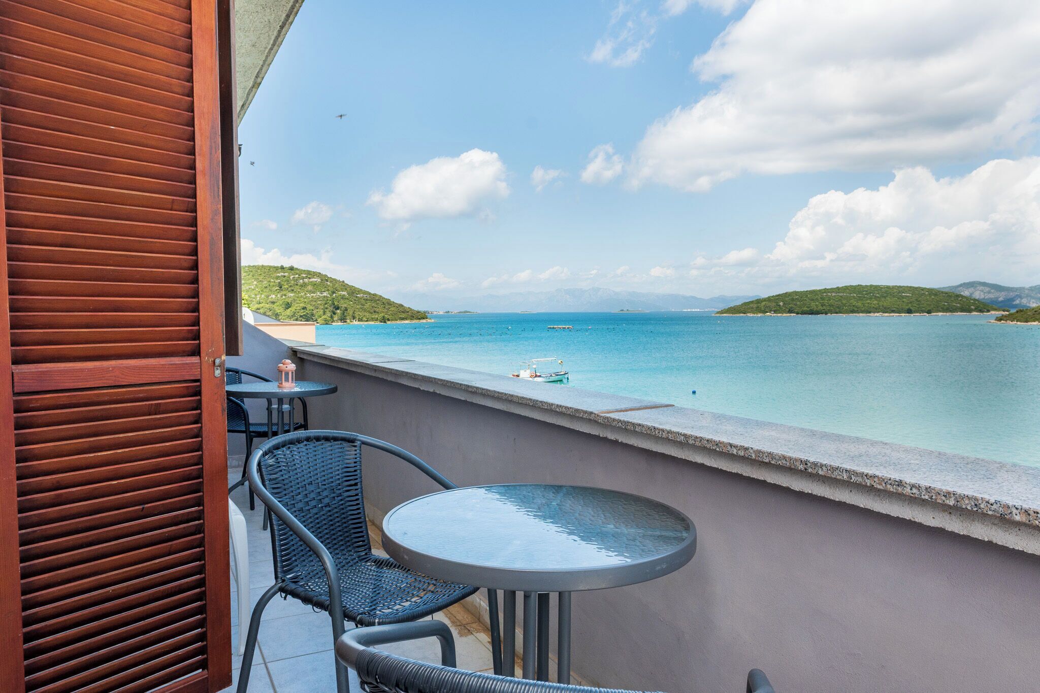 Un balcone con tavolo e sedie, affacciato su uno specchio d'acqua e una verde collina in lontananza.