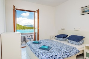 Un dormitorio con cama, dos almohadas, una mesita de noche, un escritorio, una silla y una ventana con vistas al paisaje.