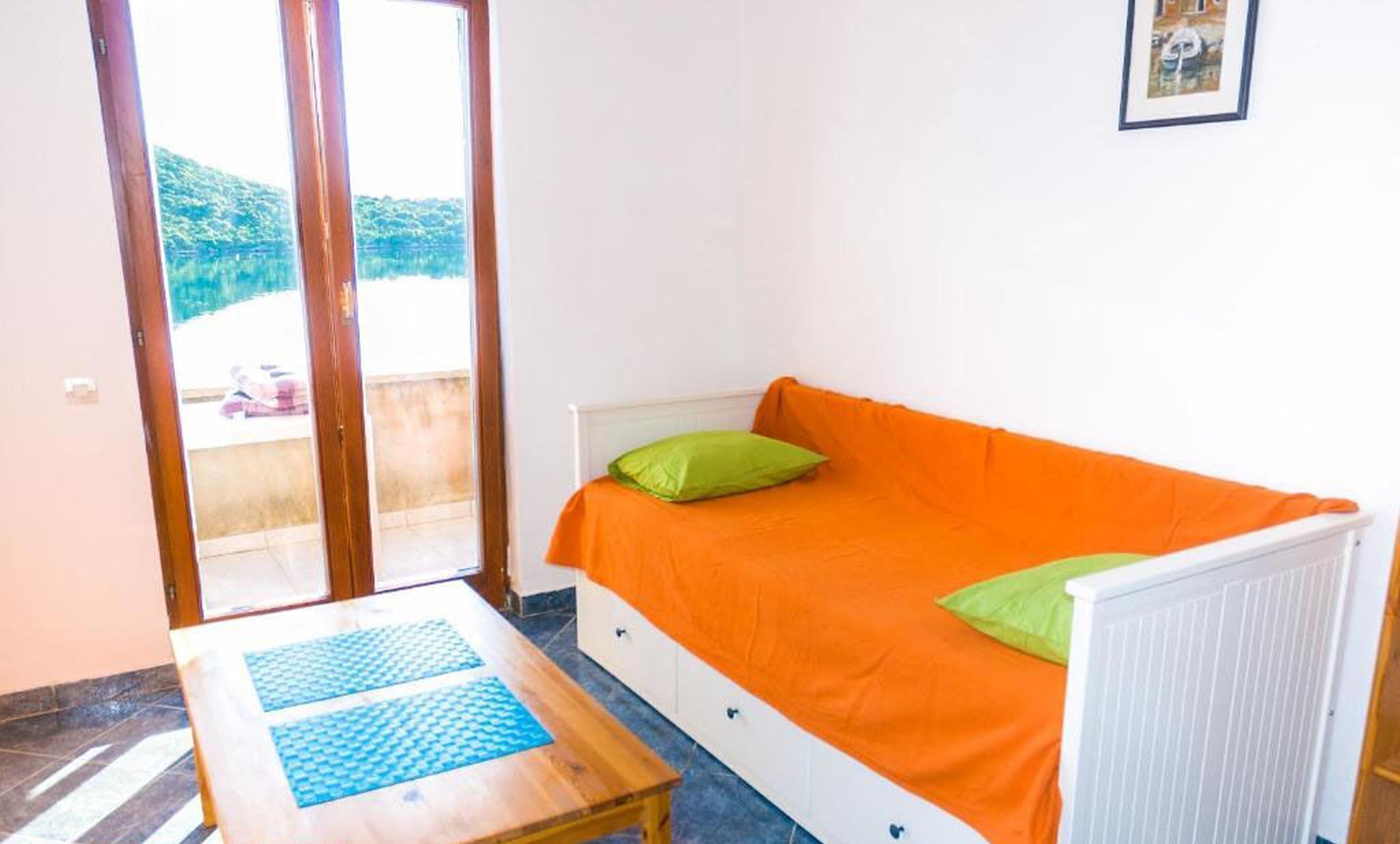 Ein kleines Zimmer mit Bett, Tisch und Blick auf eine grüne Landschaft durch eine Glastür.