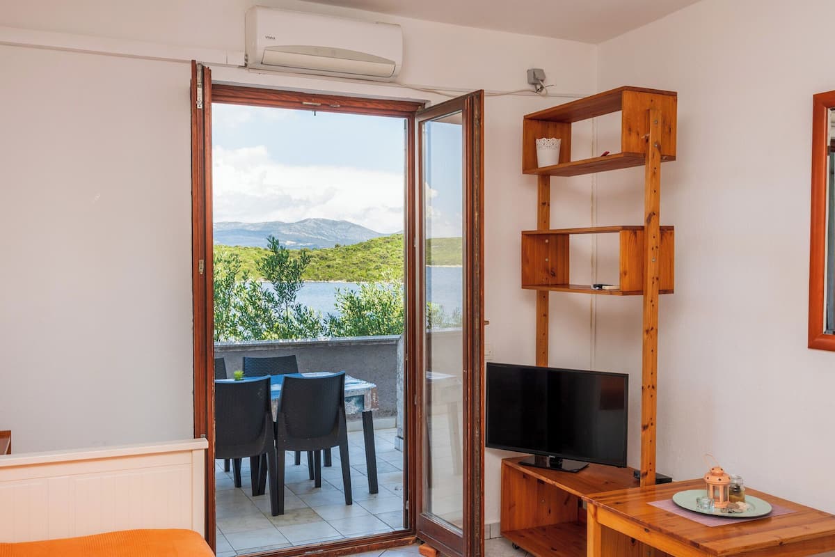 A room with a sliding glass door leading to a balcony, a wooden TV stand, and a table with chairs.