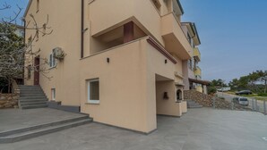 A multi-story building with a flat roof, a stone wall, and a paved courtyard. - Apartments and Rooms Rakic (Mali Losinj)