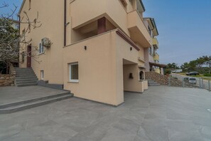 A multi-story building with a flat roof, a stone wall, and a paved courtyard. - Apartments and Rooms Rakic (Mali Losinj)