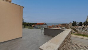 A rooftop terrace with a stone wall, a metal railing, and a view of the sea and buildings. - Apartments and Rooms Rakic (Mali Losinj)