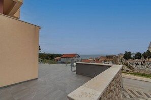 A rooftop terrace with a stone wall, a metal railing, and a view of the sea and buildings. - Apartments and Rooms Rakic (Mali Losinj)