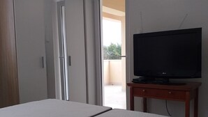 A bedroom with a bed, a TV on a wooden stand, a wardrobe, and a door leading to a balcony. - Apartments and Rooms Rakic (Mali Losinj)
