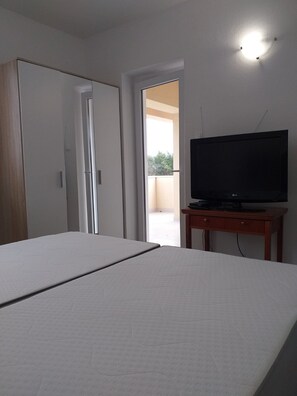 A bedroom with a bed, a TV on a wooden stand, a wardrobe, and a door leading to a balcony. - Apartments and Rooms Rakic (Mali Losinj)