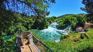 A wooden bridge leading to a waterfall, surrounded by lush greenery and a stone building. - Apartment Skatula Skradin (Skradin)