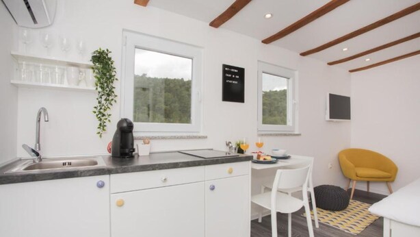 A modern kitchen with a sink, a coffee machine, and a dining area with a white table and chairs. - Apartment Skatula Skradin (Skradin)