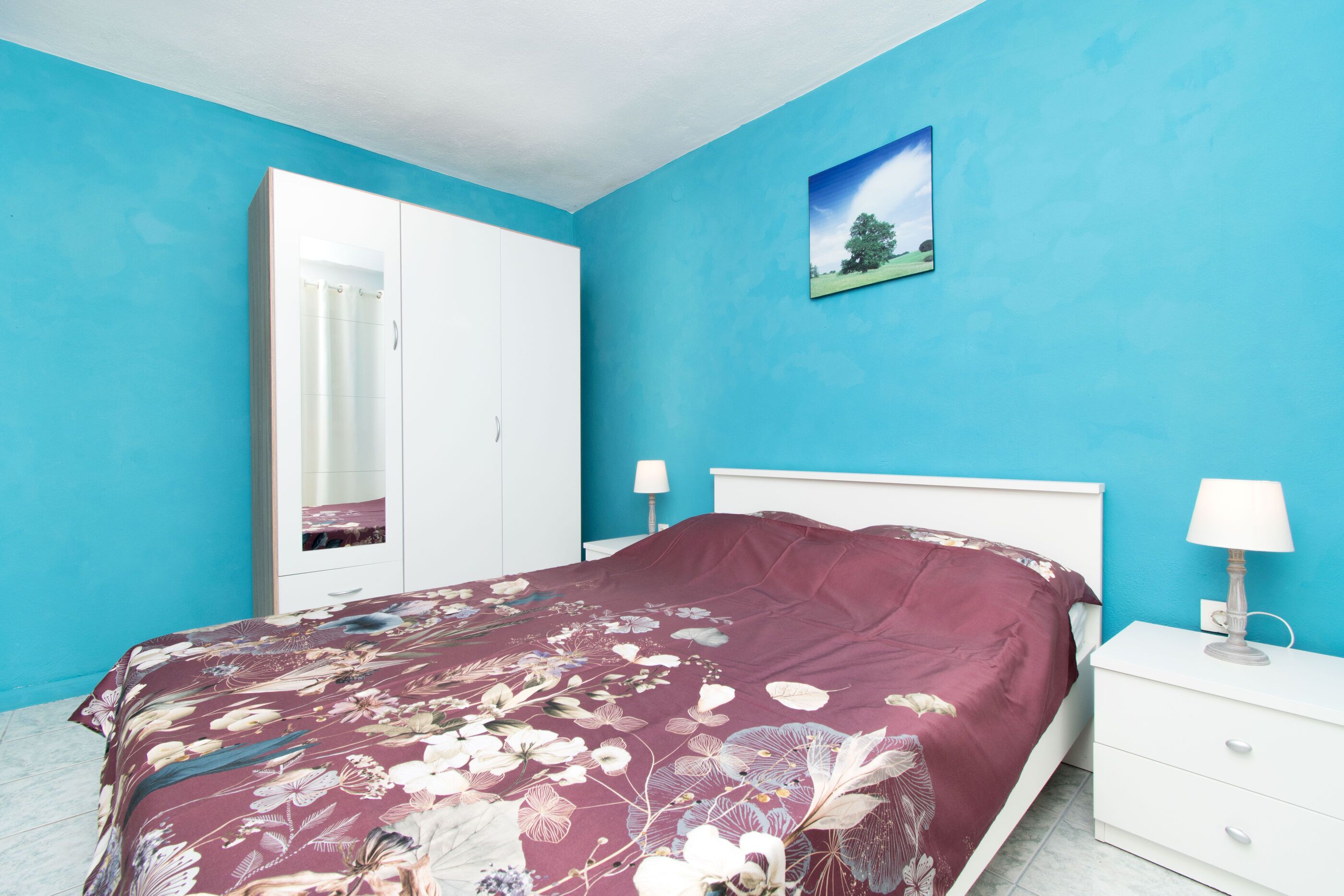 A bedroom with a bed, a nightstand, a dresser, and a picture on the wall.