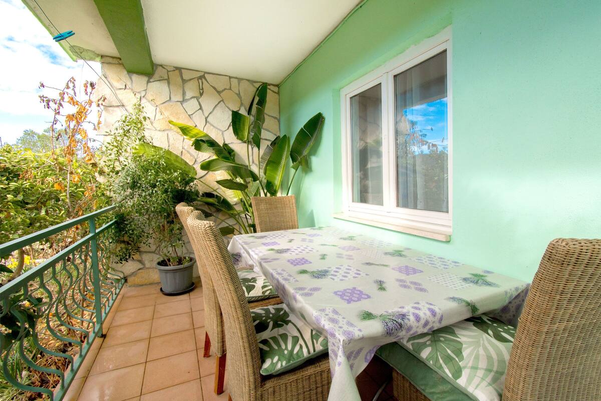 A balcony with wicker furniture, a table with a floral tablecloth, potted plants, and a stone wall.