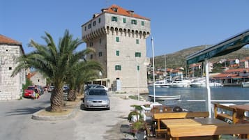A coastal town with a prominent stone tower, a marina with boats, and outdoor seating by the water.