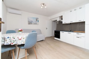 A modern kitchen with white cabinets, a dining area with a floral tablecloth, and a sofa. - Apartments Mirkovic (Marina)