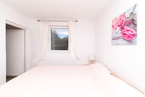 A bedroom with a bed, a window with curtains, a bedside table with a lamp, and a wall-mounted picture. - Apartments Mirkovic (Marina)