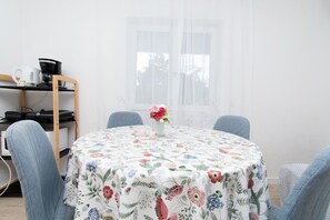 A round table with a floral tablecloth, two chairs, a vase with flowers, and a coffee maker on a shelf. - Apartments Mirkovic (Marina)