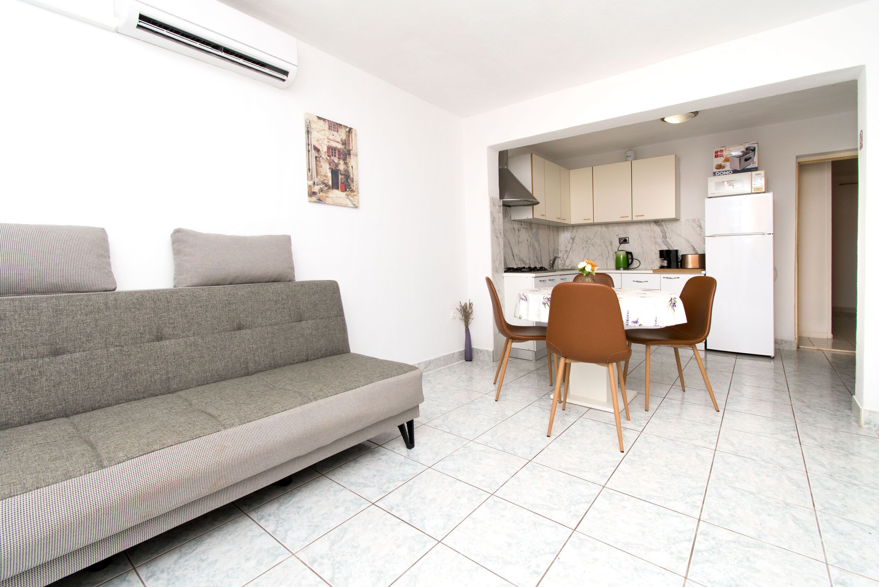 Ein modernes Wohnzimmer mit einer Couch, einem Esstisch, Stühlen und einer Küchenzeile mit Schränken und Geräten.
