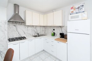 Eine Küche mit weißen Schränken, einem Gasherd, einer Spüle, einer Edelstahl-Dunstabzugshaube, einer Mikrowelle und einem Kühlschrank.