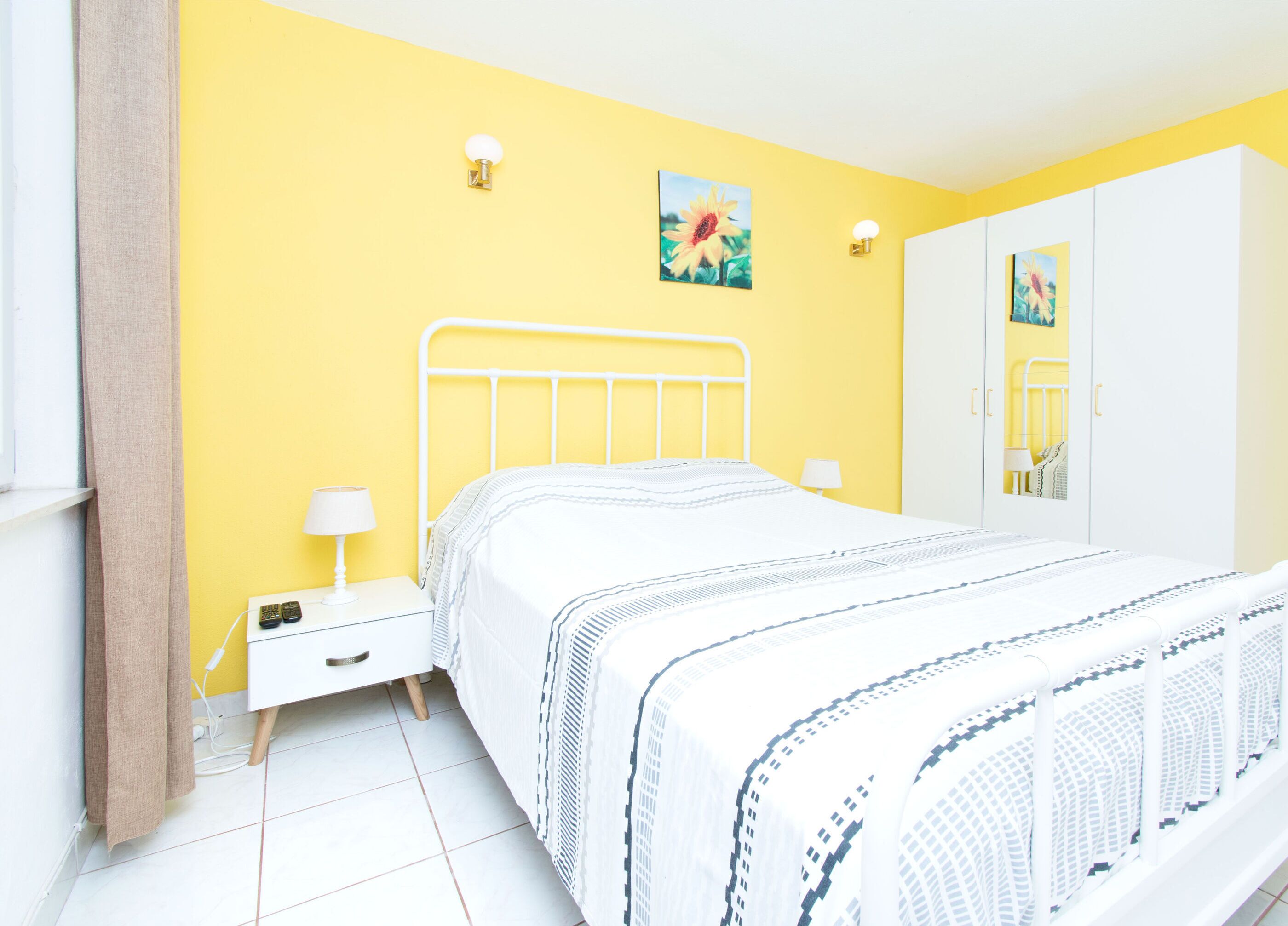 A bedroom with a bed, bedside tables, a mirror, and a yellow wall.