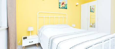 A bedroom with a bed, bedside tables, a mirror, and a yellow wall.