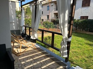 A covered outdoor area with a stone floor, wooden chairs, and a view of a residential building. - Apartments Angels Anna i Marlen (Pula)