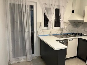 A kitchen with a white countertop, a sink, a stove, and a window with sheer curtains. - Apartments Angels Anna i Marlen (Pula)