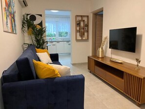A living room with a dark blue sofa, a flat-screen TV, and a wooden entertainment unit. - Apartments Angels Anna i Marlen (Pula)