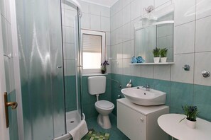 A bathroom with a glass shower enclosure, a toilet, a sink, and a mirror. - Apartment Igor (Vodice)