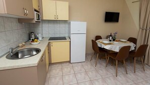 A compact kitchen with a sink, microwave, and refrigerator, a dining area with a table and chairs, and a TV mounted on the wall. - Apartment Armina (Vodice)