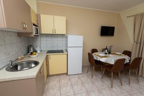 Eine kompakte Küche mit Spüle, Mikrowelle und Kühlschrank, ein Essbereich mit Tisch und Stühlen sowie ein an der Wand befestigter Fernseher.