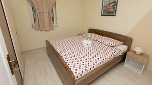 A bedroom with a bed, a nightstand, a window with curtains, and a painting on the wall. - Apartment Armina (Vodice)