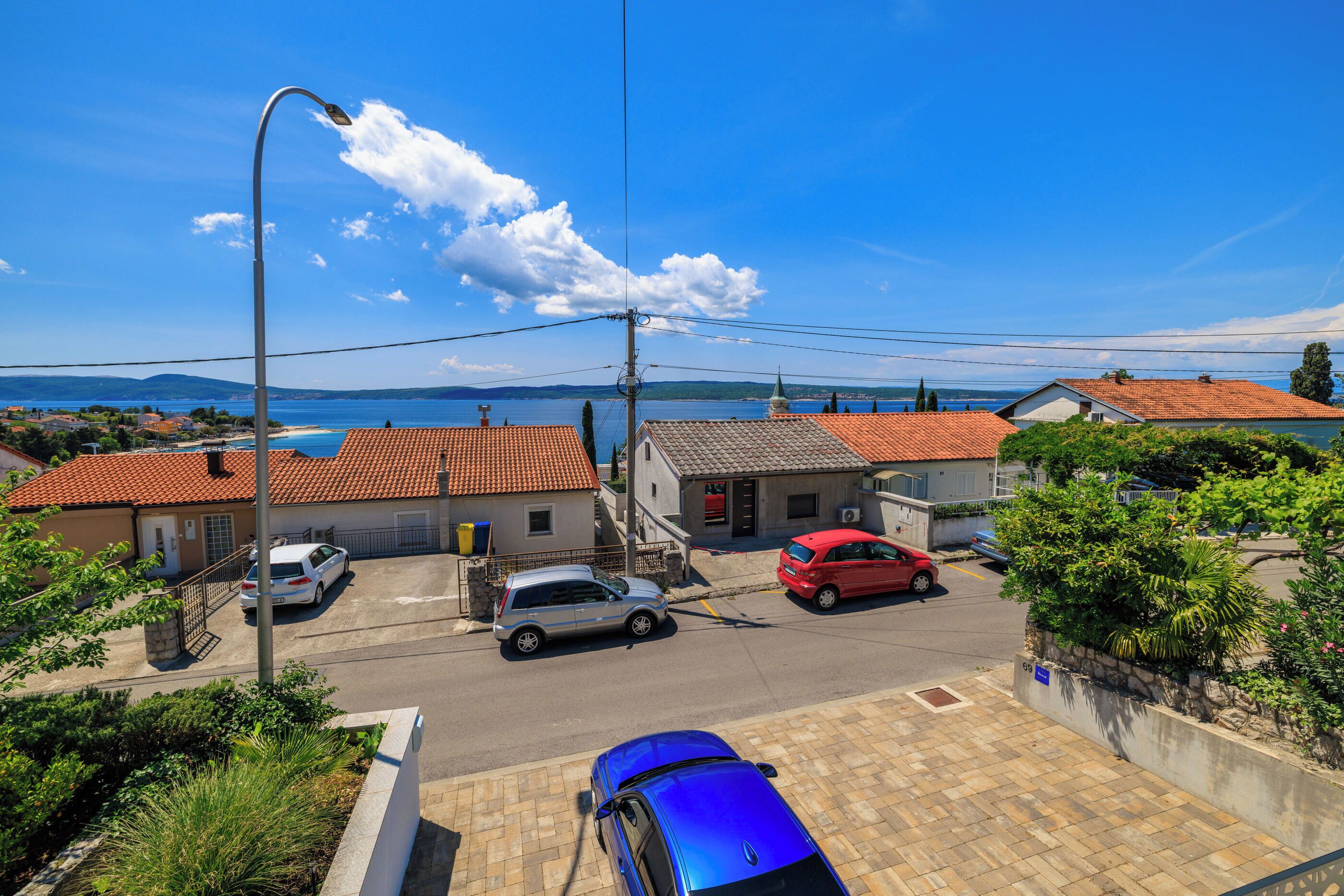 Eine Wohnstraße mit Häusern, blauem Himmel und weiter Wasserfläche im Hintergrund.