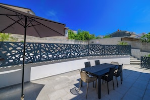 Eine Terrasse im Freien mit Tisch, Stühlen, einem großen Sonnenschirm und einem dekorativen Zaun.