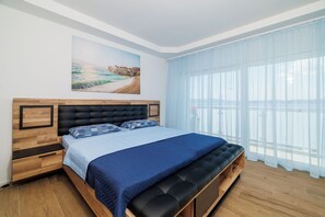 Ein Schlafzimmer mit Bett, Bank, Nachttisch, Schublade, einem Fenster mit Vorhängen und einem Bild an der Wand.
