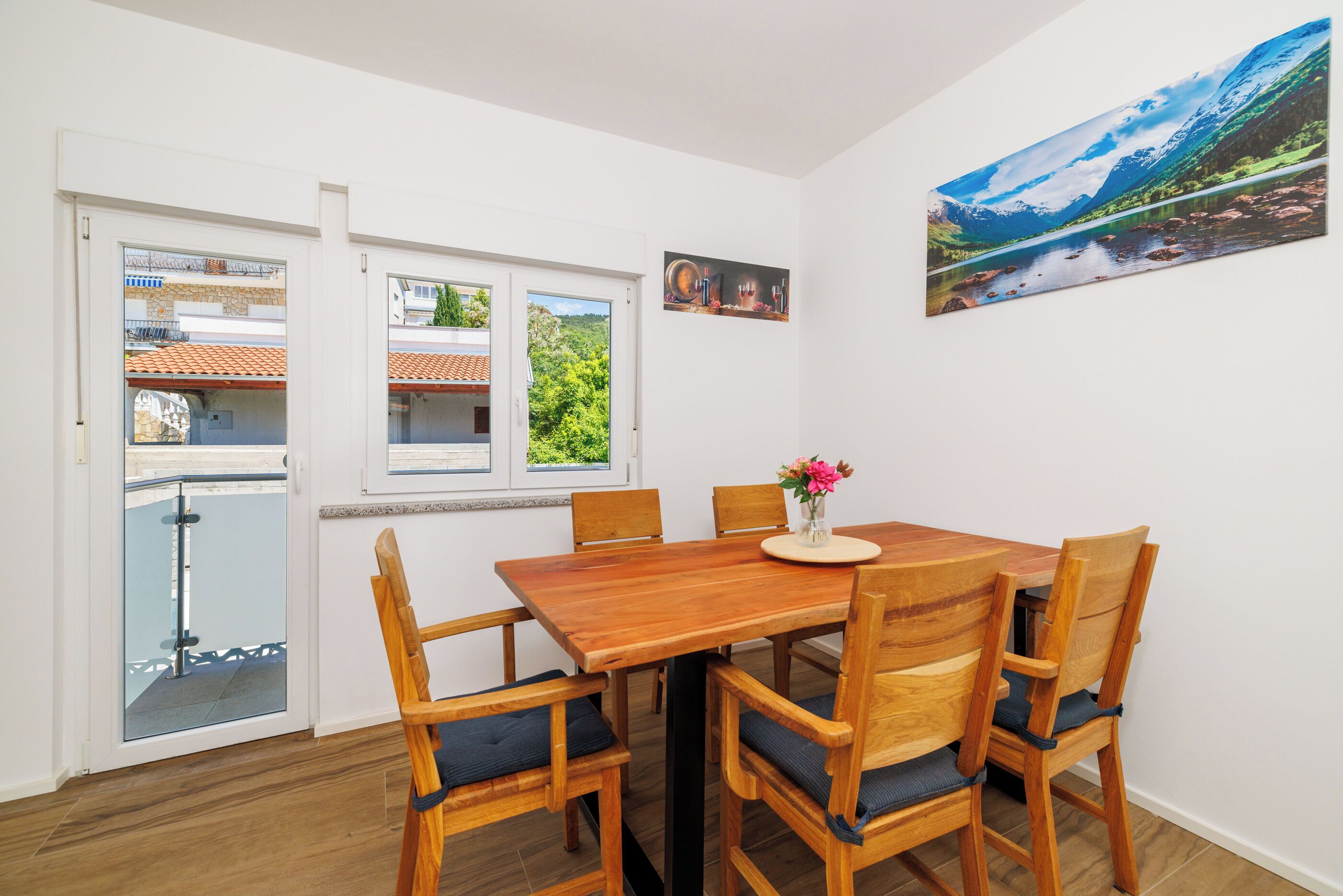 Un coin repas avec une table et des chaises en bois, un vase rempli de fleurs et un tableau accroché au mur.