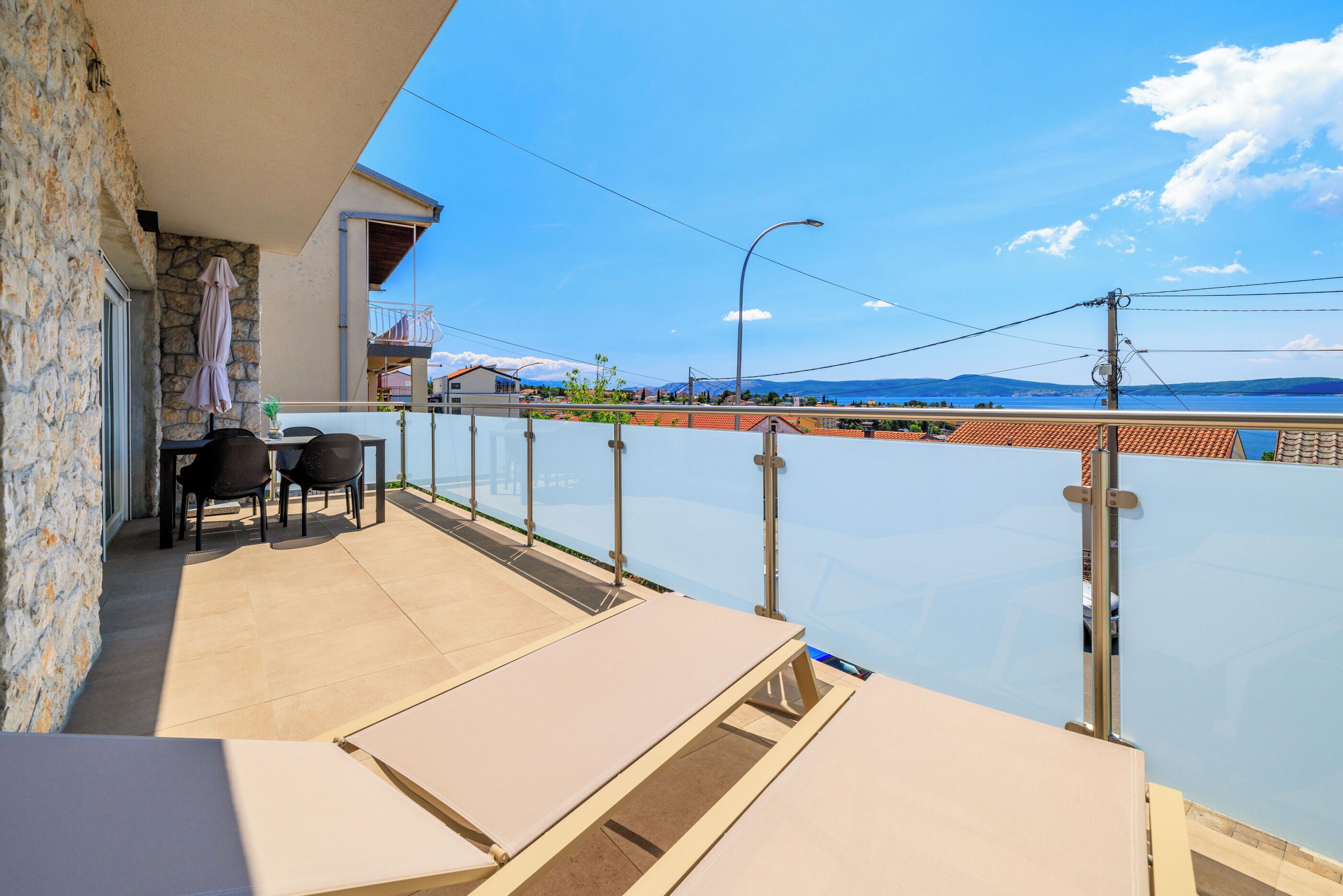 A balcony with a view of the sea, a table with chairs, and a stone wall.