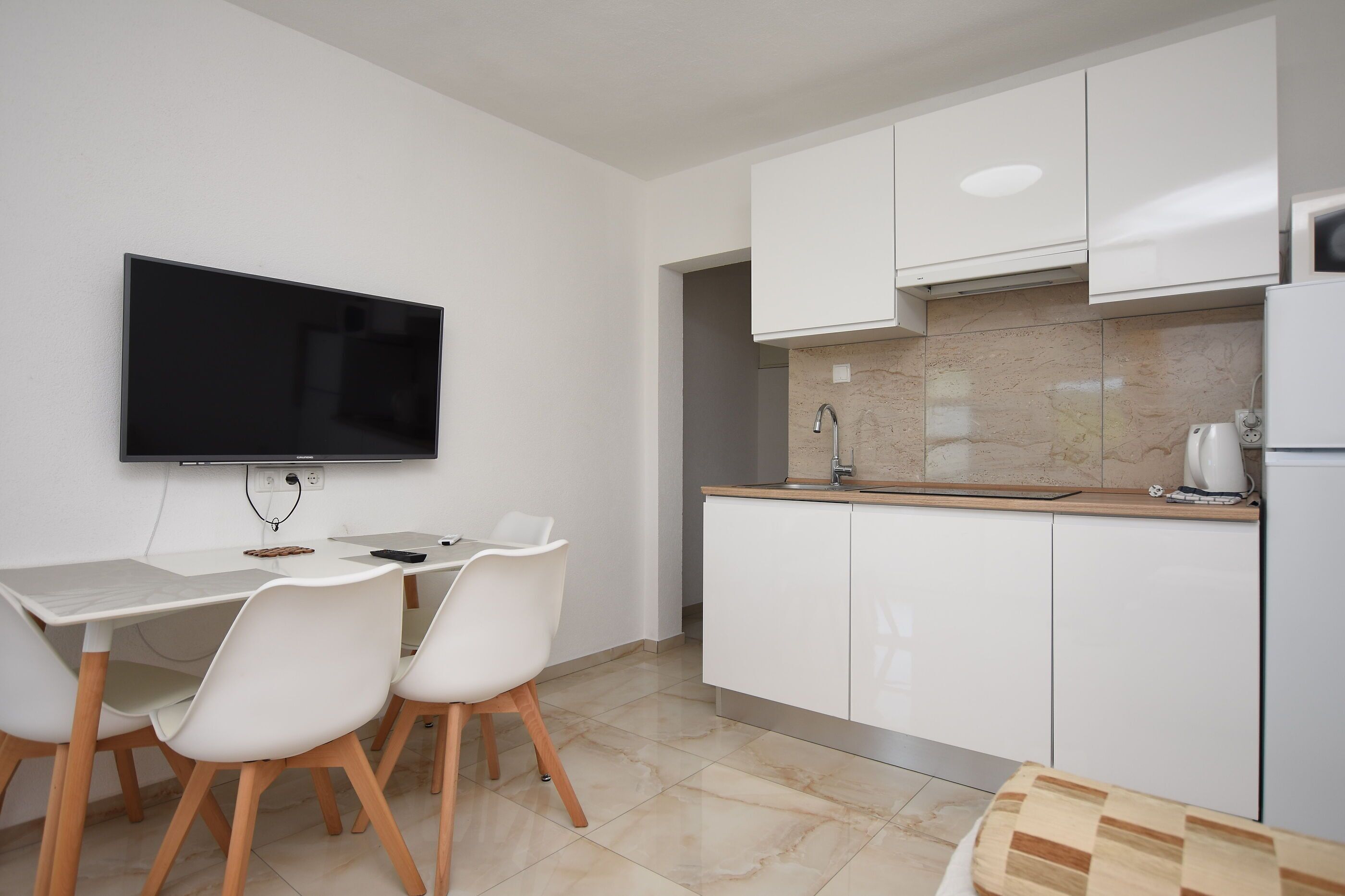 Cozinha moderna com armários brancos, uma TV de tela plana e um espaço de refeições com cadeiras brancas.