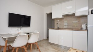 A modern kitchen with white cabinets, a flat-screen TV, and a dining area with white chairs. - Apartments Relax (Obrovac)