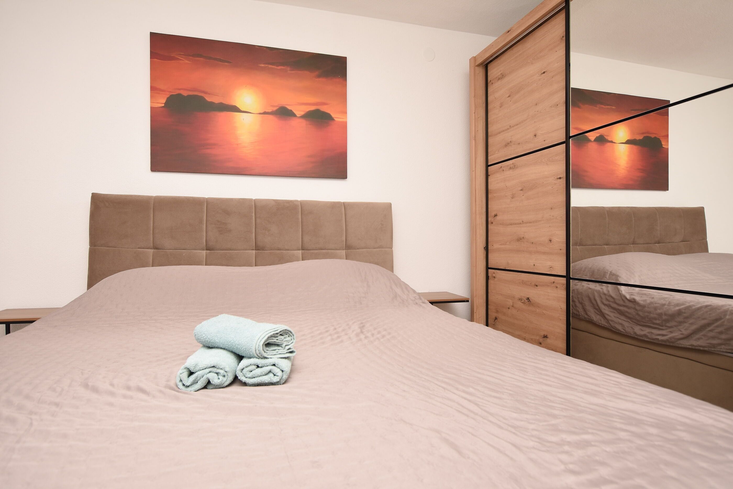 Um quarto com cama, guarda-roupa de madeira e uma pintura do pôr do sol na parede.