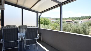 A covered balcony with a table and chairs, overlooking a residential area with trees and houses. - Apartments Relax (Obrovac)