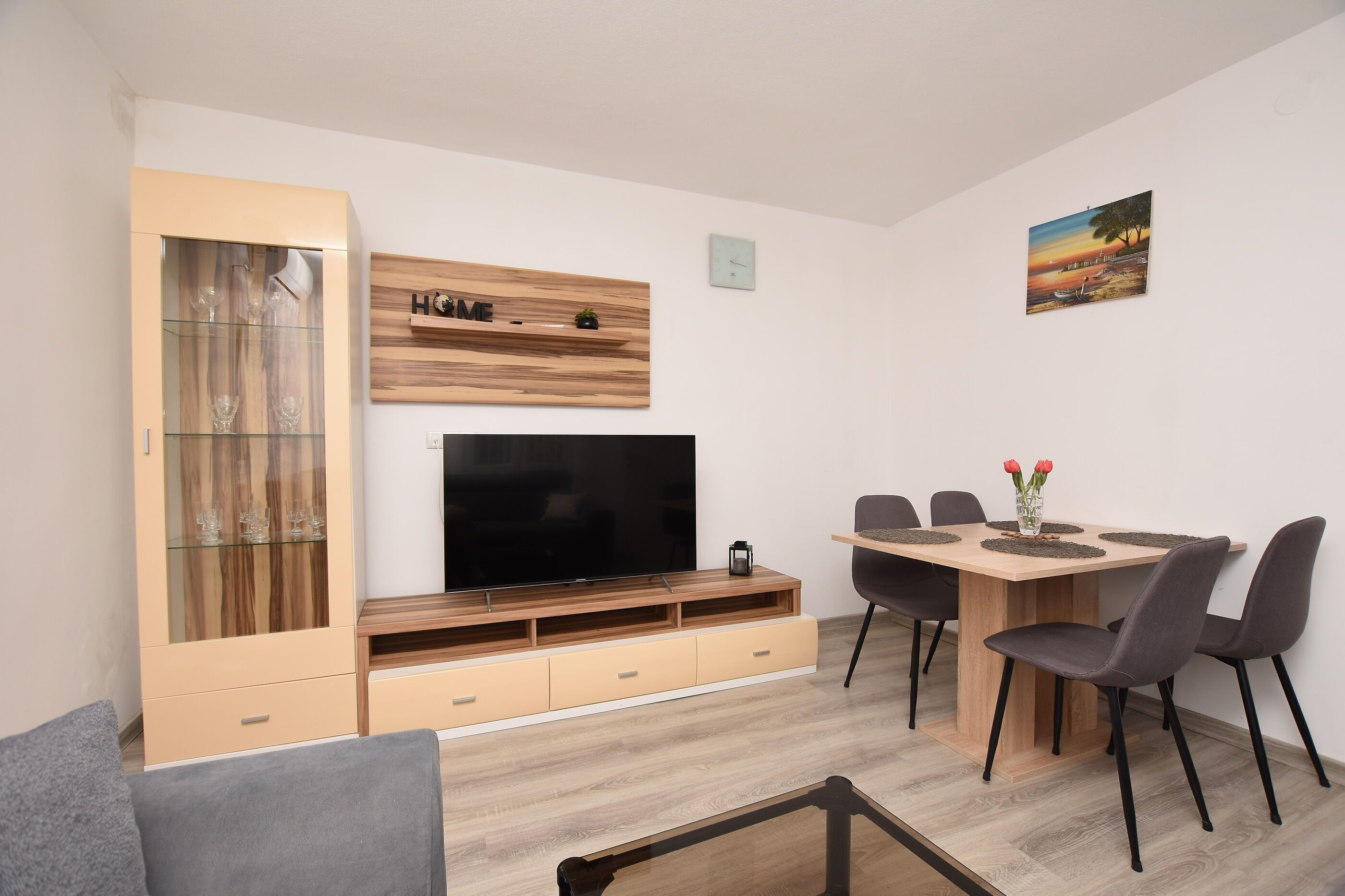 A modern living room with a TV, wooden cabinet, dining table, and chairs.