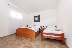 Ein Zimmer mit zwei Holzbett, einem Nachttisch, einem Wandbild und einem Fenster mit Vorhängen.