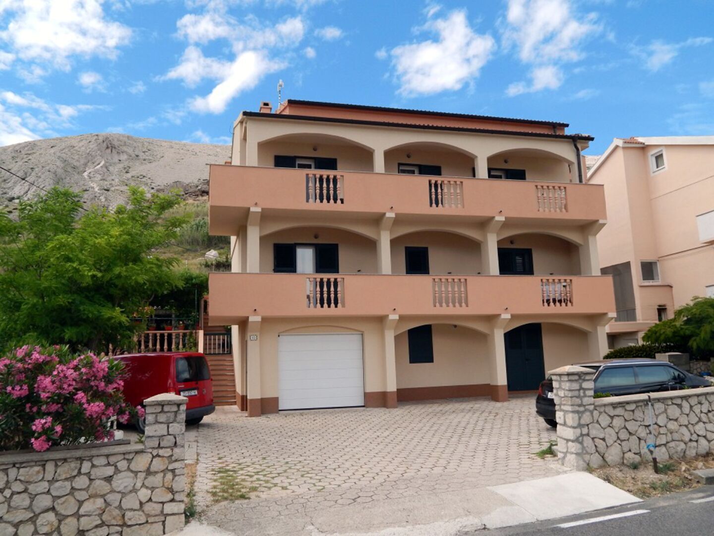 Ein mehrstöckiges Wohngebäude mit Balkonen, einer Garage und einer Steinmauer.