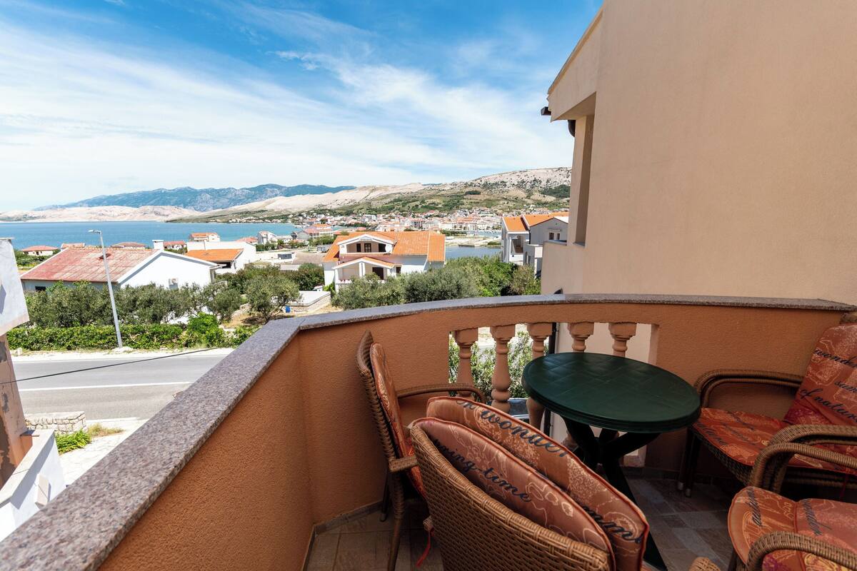Un balcon agrémenté de meubles en osier, d’une table et offrant une vue sur une ville côtière.